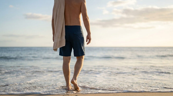 Persona con un short de baño de talle alto caminando hacia el mar en la orilla de una playa