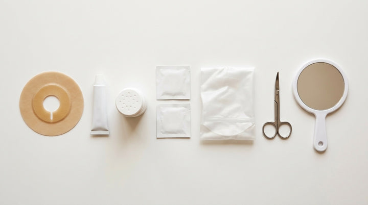 Accesorios para el cambio de bolsa de colostomía ordenados en fila: barrera recortable, pasta, polvo, toallitas, bolsa, tijeras curvas y espejo de mano