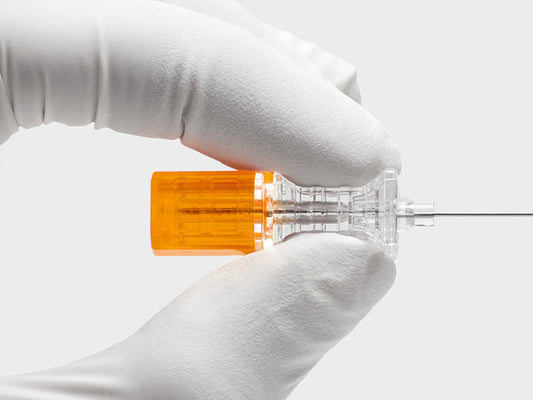 Hub transparente de aguja espinal B. Braun Pencan con estilete naranja, sujetado con guante